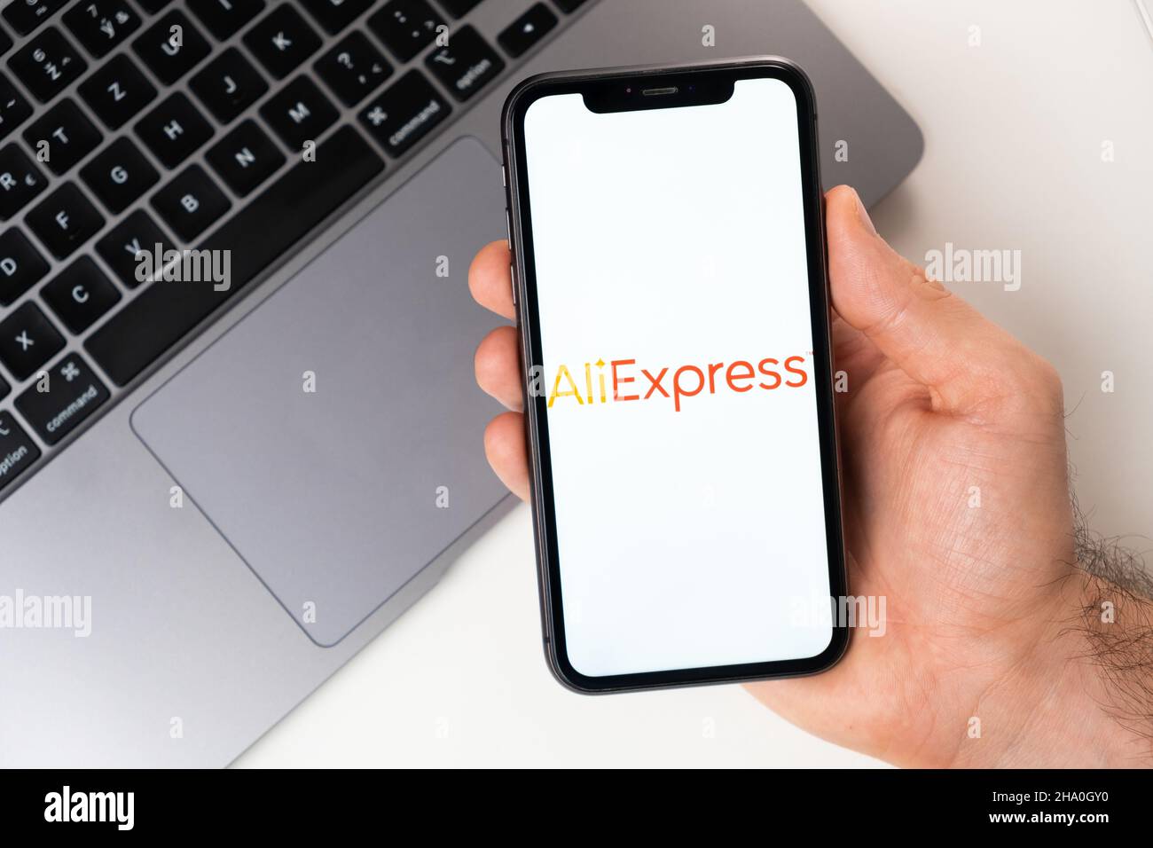 AliExpress mobile application on the smartphone screen. A mobile phone in a man hand near an open laptop. White background. November 2021, San Francisco, USA Stock Photo