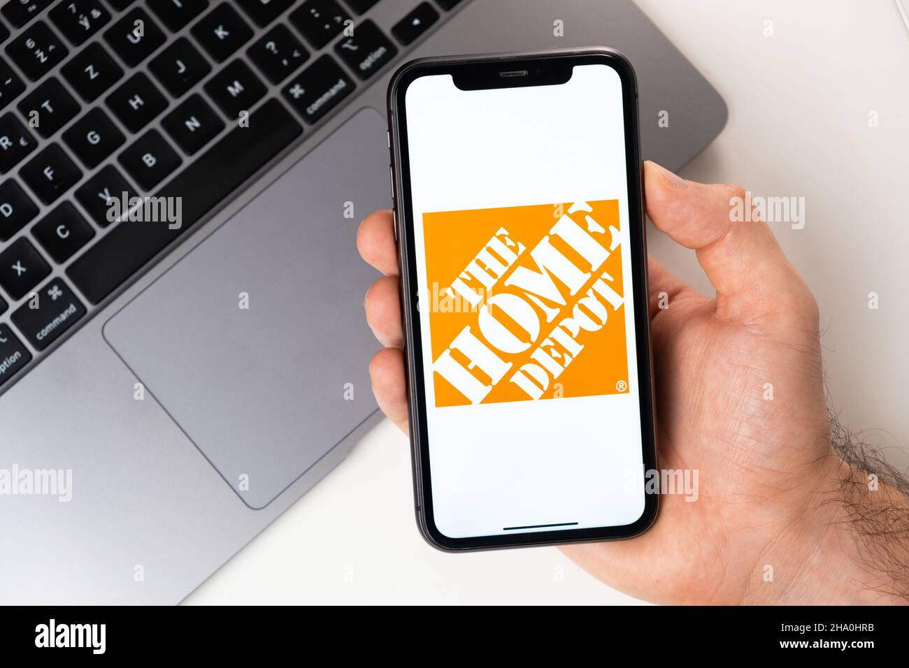 The home depot mobile application on the smartphone screen. A mobile phone in a man hand near an open laptop. White background. November 2021, San Francisco, USA Stock Photo