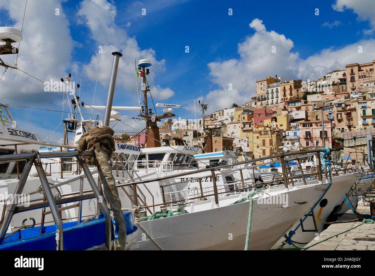Sciacca, Sicily, Italy, 24.03.2018. Fishing boats in harbor with colorful houses of old town in the background. Stock Photo