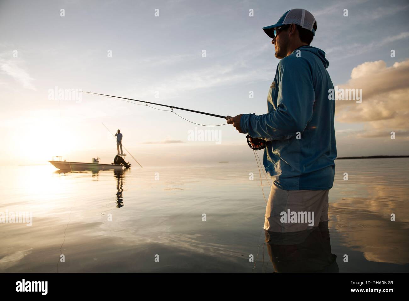 A fisherman wades while fly fishing in keys with boat in background Stock Photo