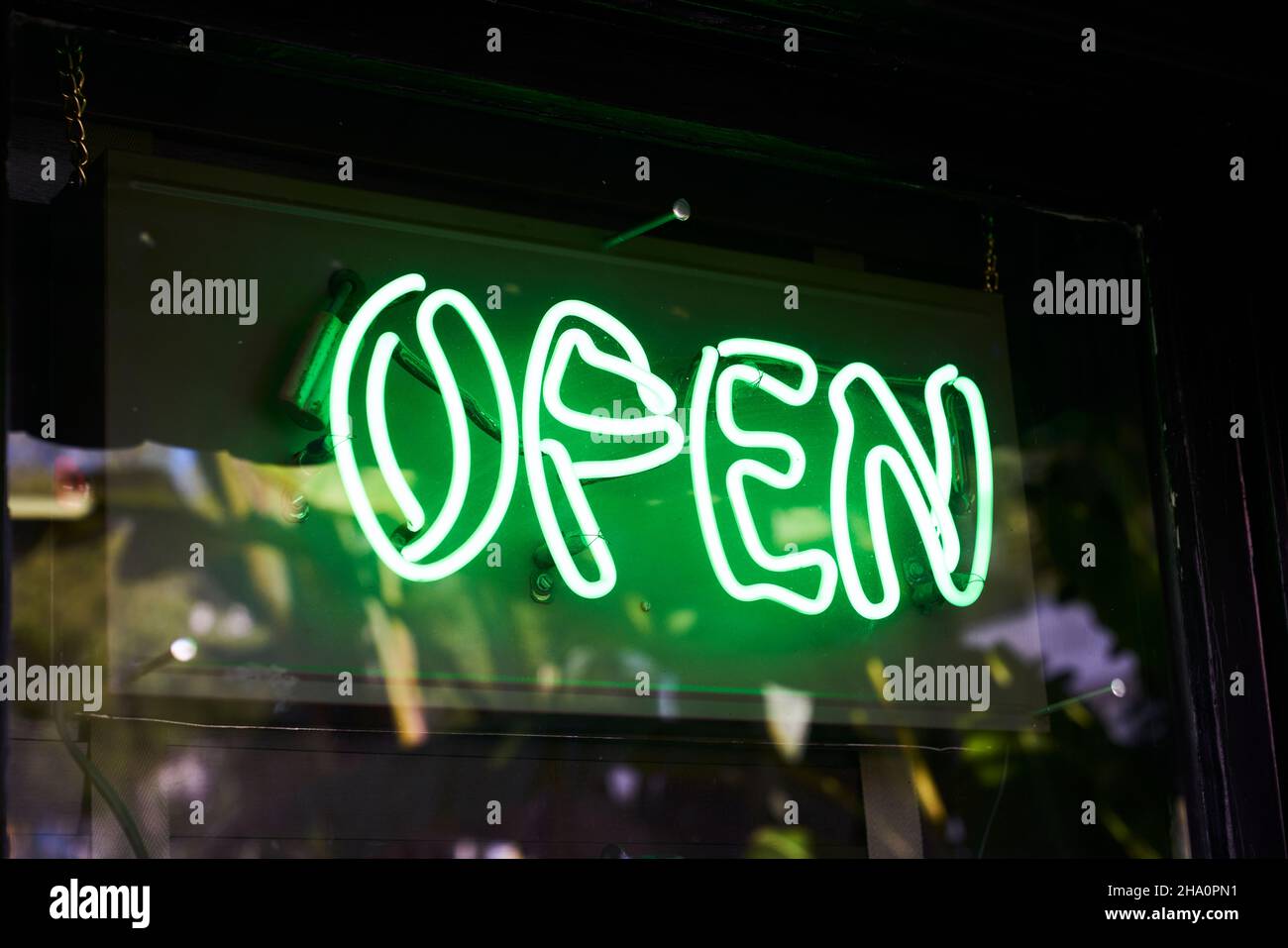 Green neon open sign hanging in a window with reflections Stock Photo