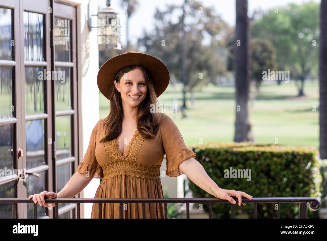 Smiling woman in brown dress & a hipster hat with hands on railing Stock Photo