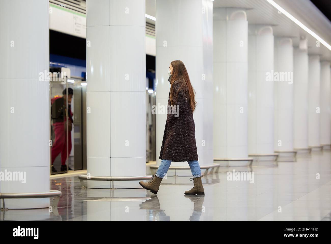 A full-length photo of a woman in a medical face mask to avoid the spread of coronavirus who is going on the subway platform. A girl in a surgical mas Stock Photo