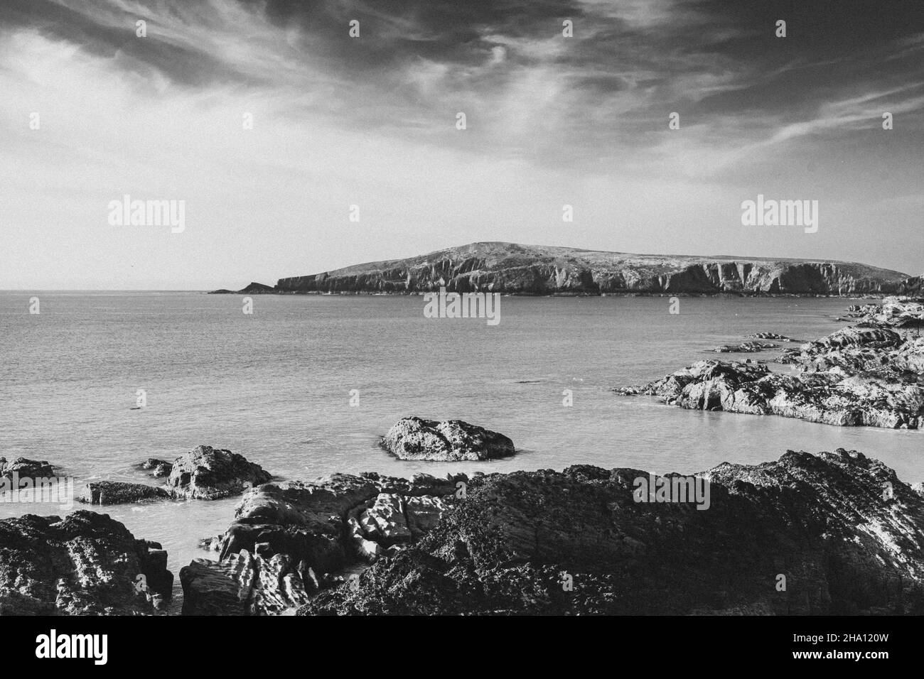 monochrome image of cardigan island seen from the rocky shoreline of gwbert west wales Stock Photo