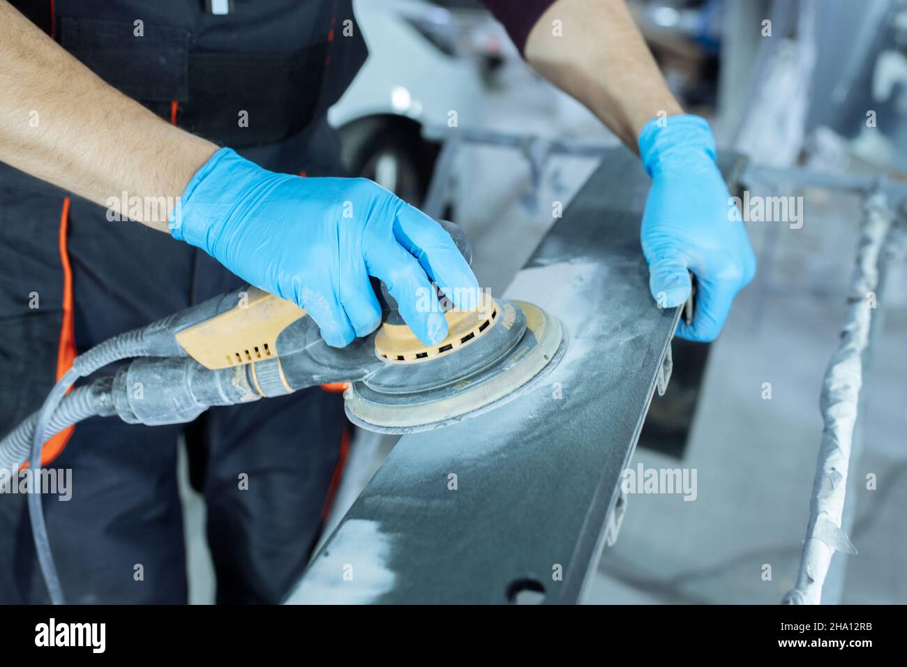 Sanding a car body part with electrical grinder machine before painting
