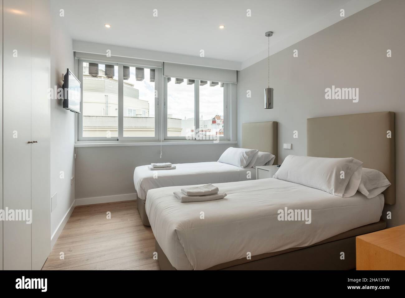 Two Separate Views Bedroom with two separate beds with towels and white cabinets, wall tv ...