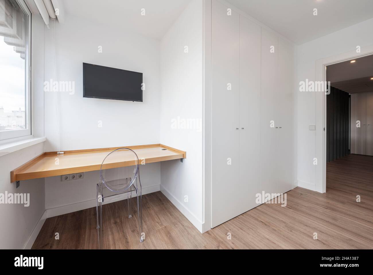 Room with desk, small plasma TV, white built-in wardrobe and oak parquet floors Stock Photo