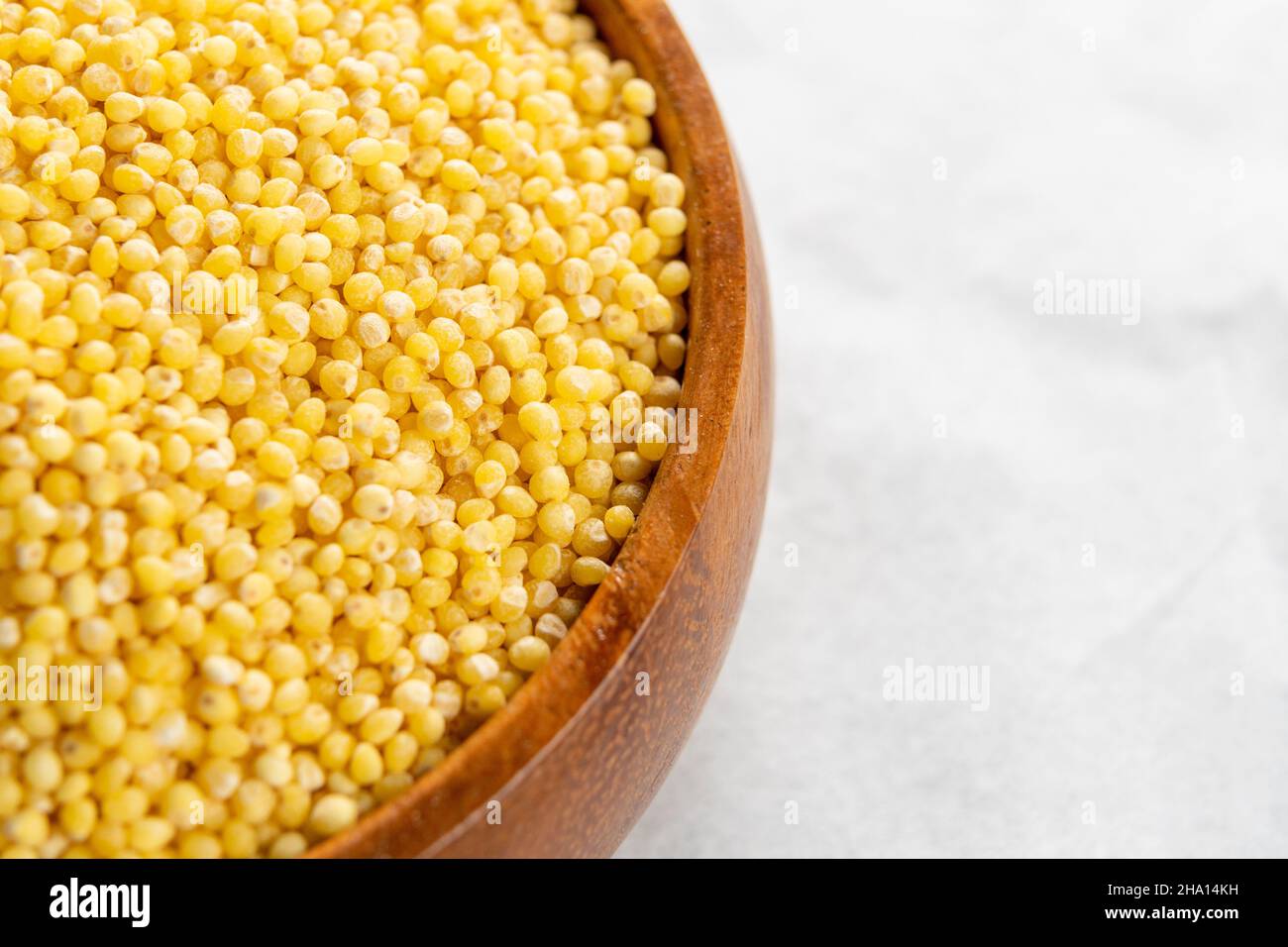 Full rustic wooden bowl with dry millet on a white tablecloth. Macro. Selective focus Stock Photo
