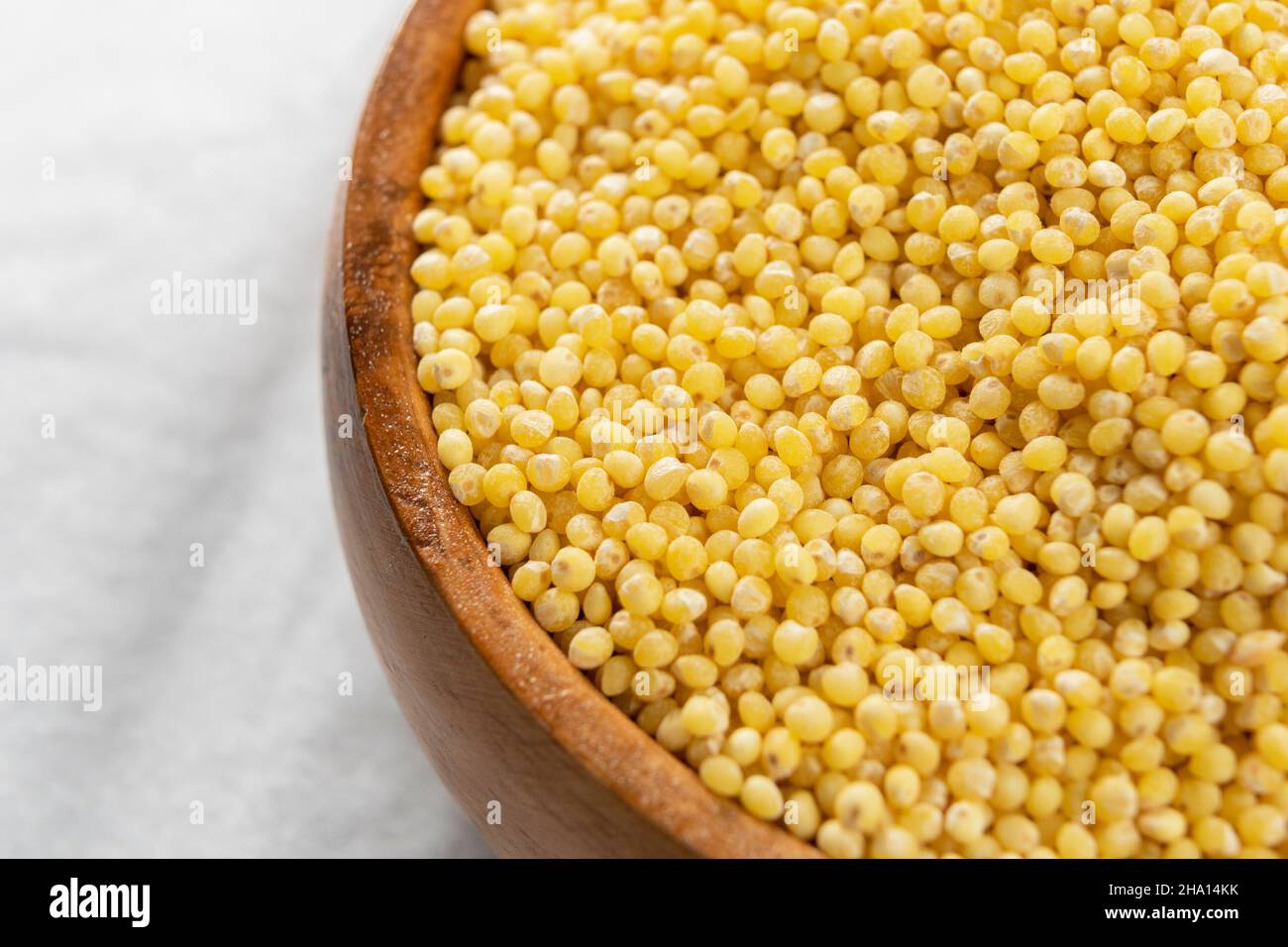Wooden bowl with uncooked millet on a white crumpled napkin. Macro. Selective focus Stock Photo