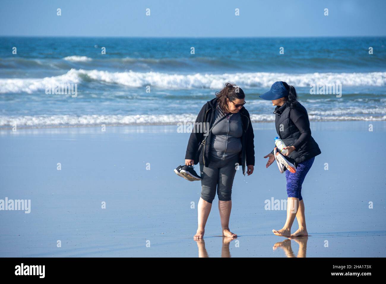 Two Mexican friends walking barefoot on the sand of Tijuana Beach, Tijuana, Mexico. Stock Photo