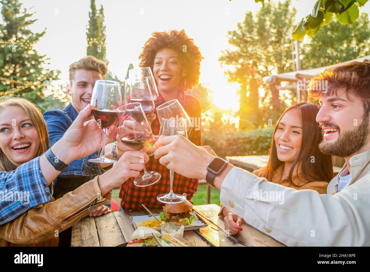 Group of multiethnic friends living healthy lifestyle and smiling and joking while drinking red wine at outdoor pub restaurant - Young people toasting Stock Photo