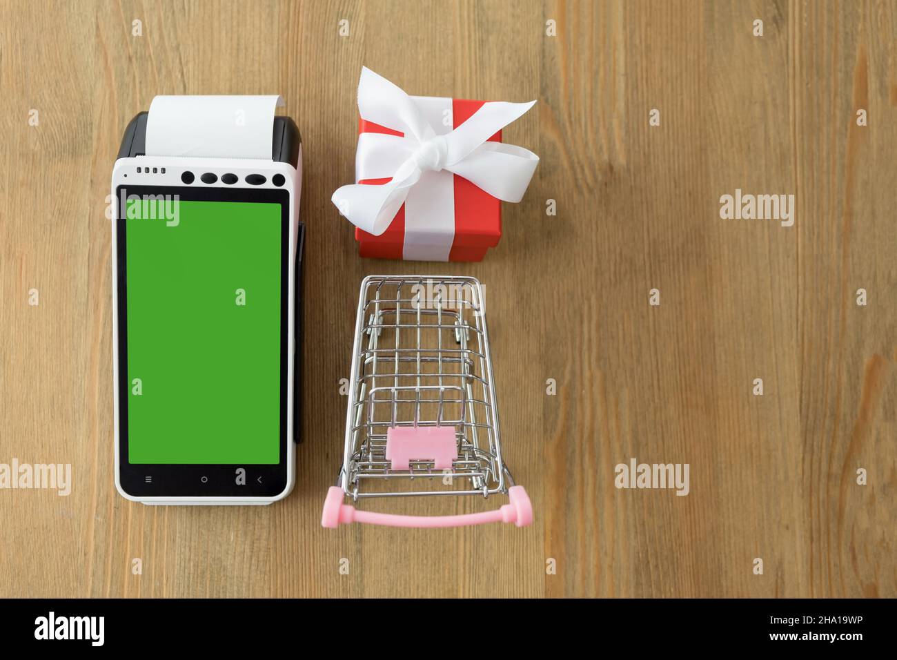 POS terminal with blank screen with miniature shopping cart and red gift box on a wooden background Stock Photo