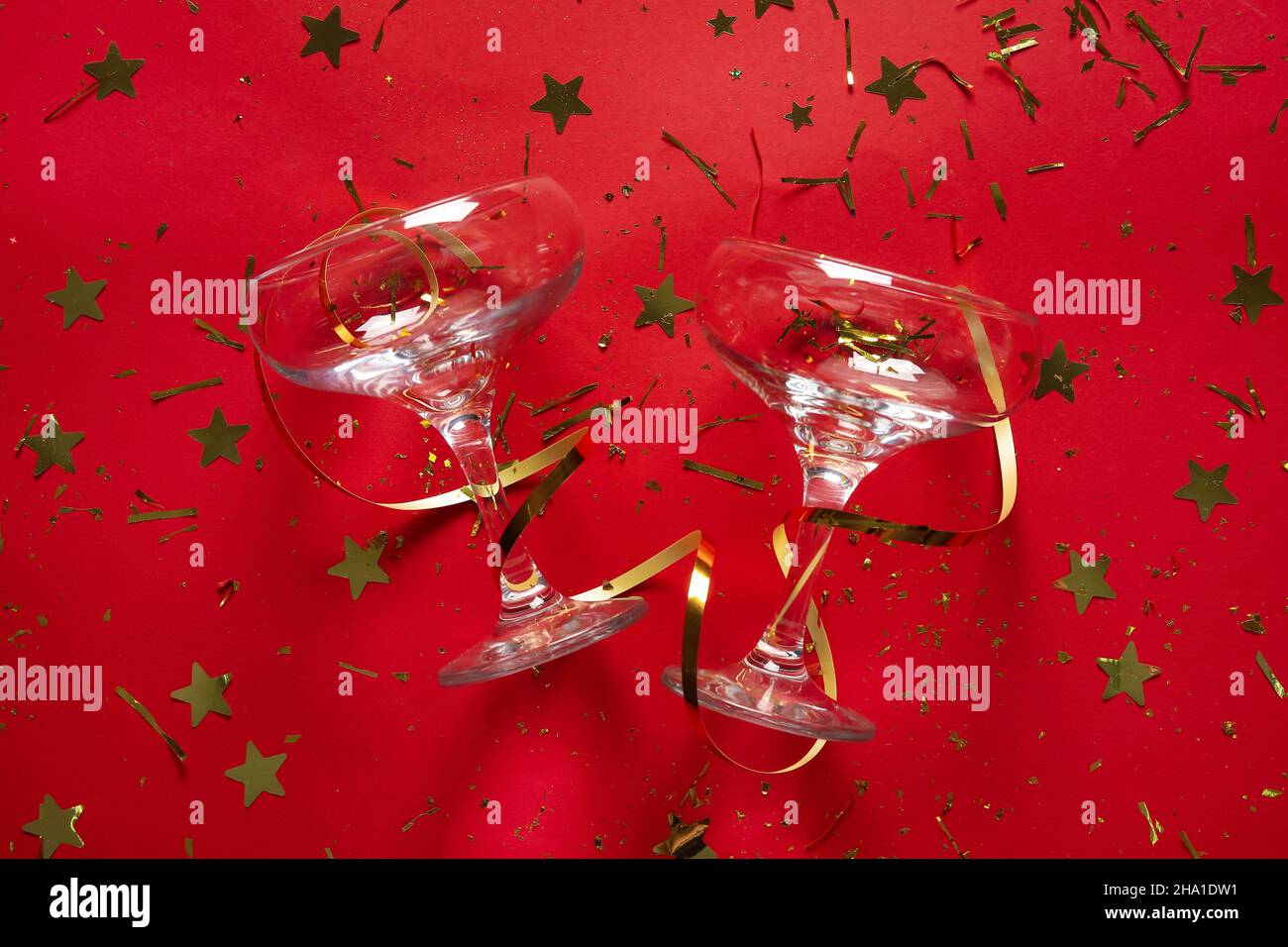 Champagne glasses, serpentine and golden confetti on red background