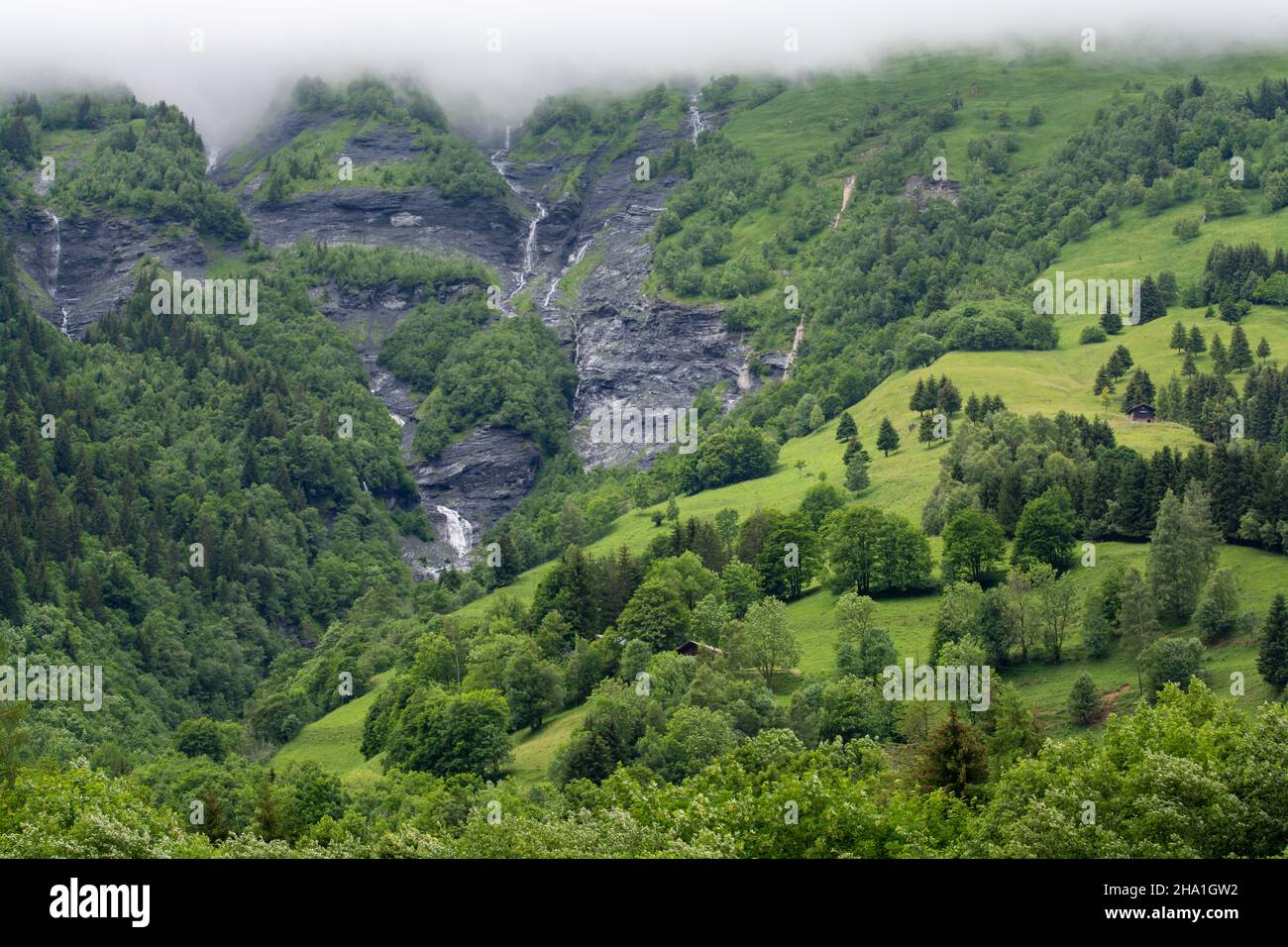Panoramic view on mountain waterfalls, green forests and apline meadows near Saint-Gervais-les-Bains, Savoy, France in summer Stock Photo