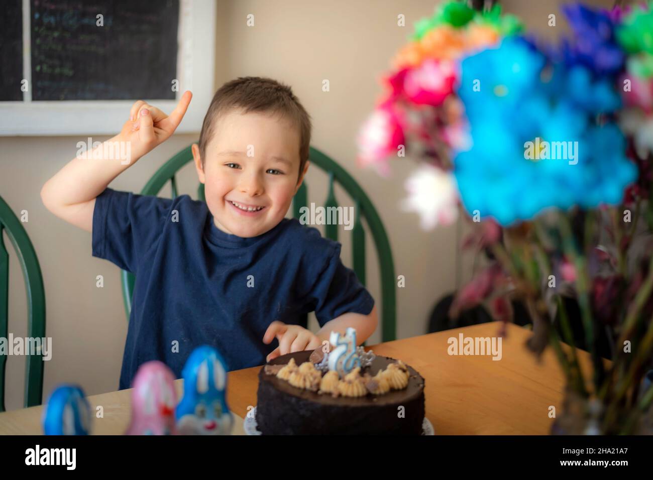 Boy celebrating his 5 years anniversary at a table with a cake and a candle in the form of figure 5 Stock Photo