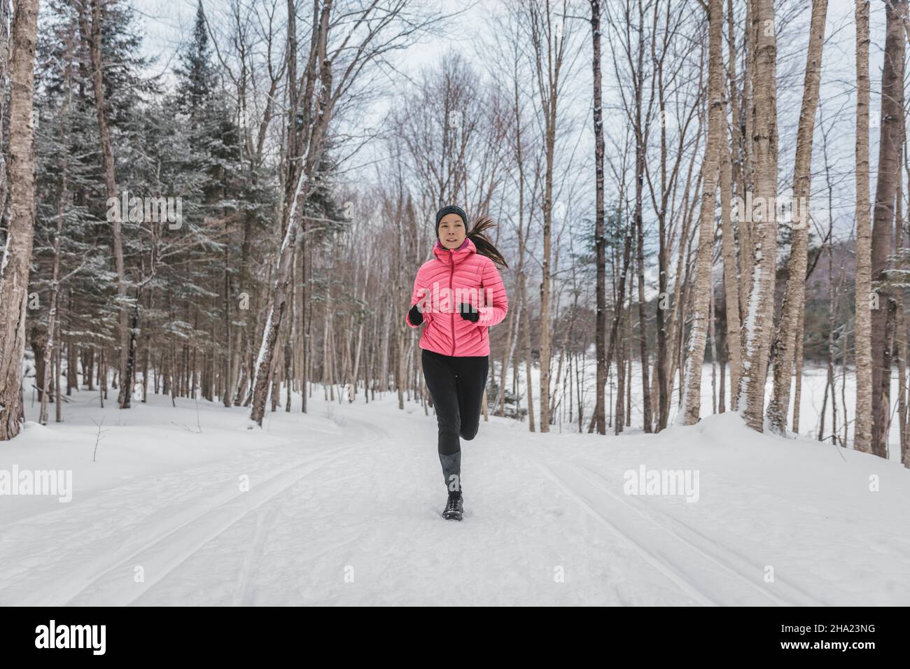 Winter Woman Running in Snow. Runner working out outside on winter day in forest. Fit healthy lifestyle picture of beautiful young sports model Stock Photo