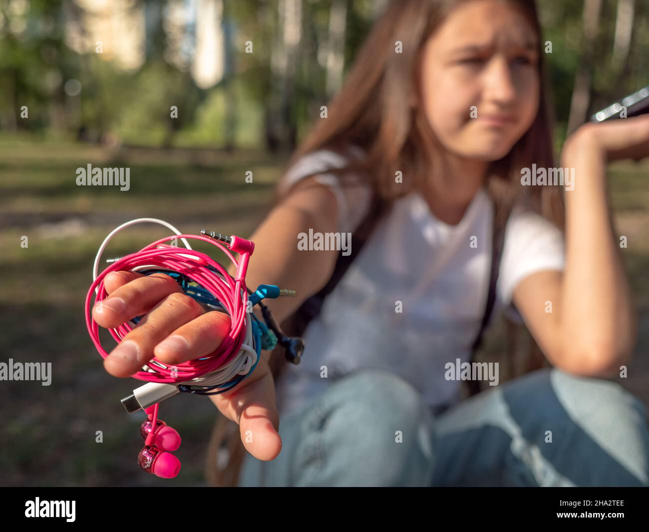 Girl with the phone and four pairs of in-ear wired colorful pink, blue, white, and black earbuds tangled around the hand. Messy wires problem, puzzled Stock Photo