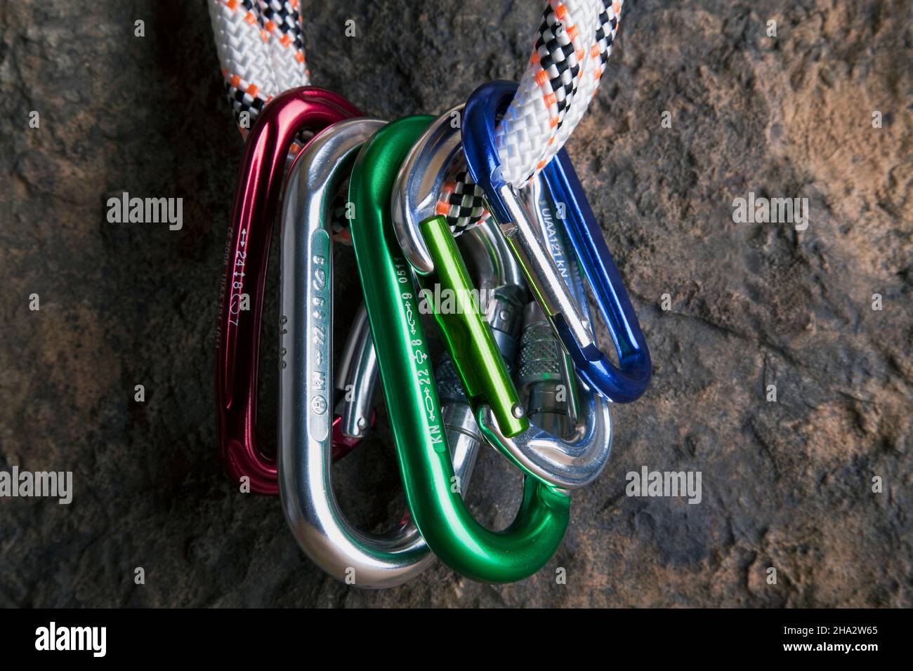 five carabiners hanging on a rope on a rock face Stock Photo