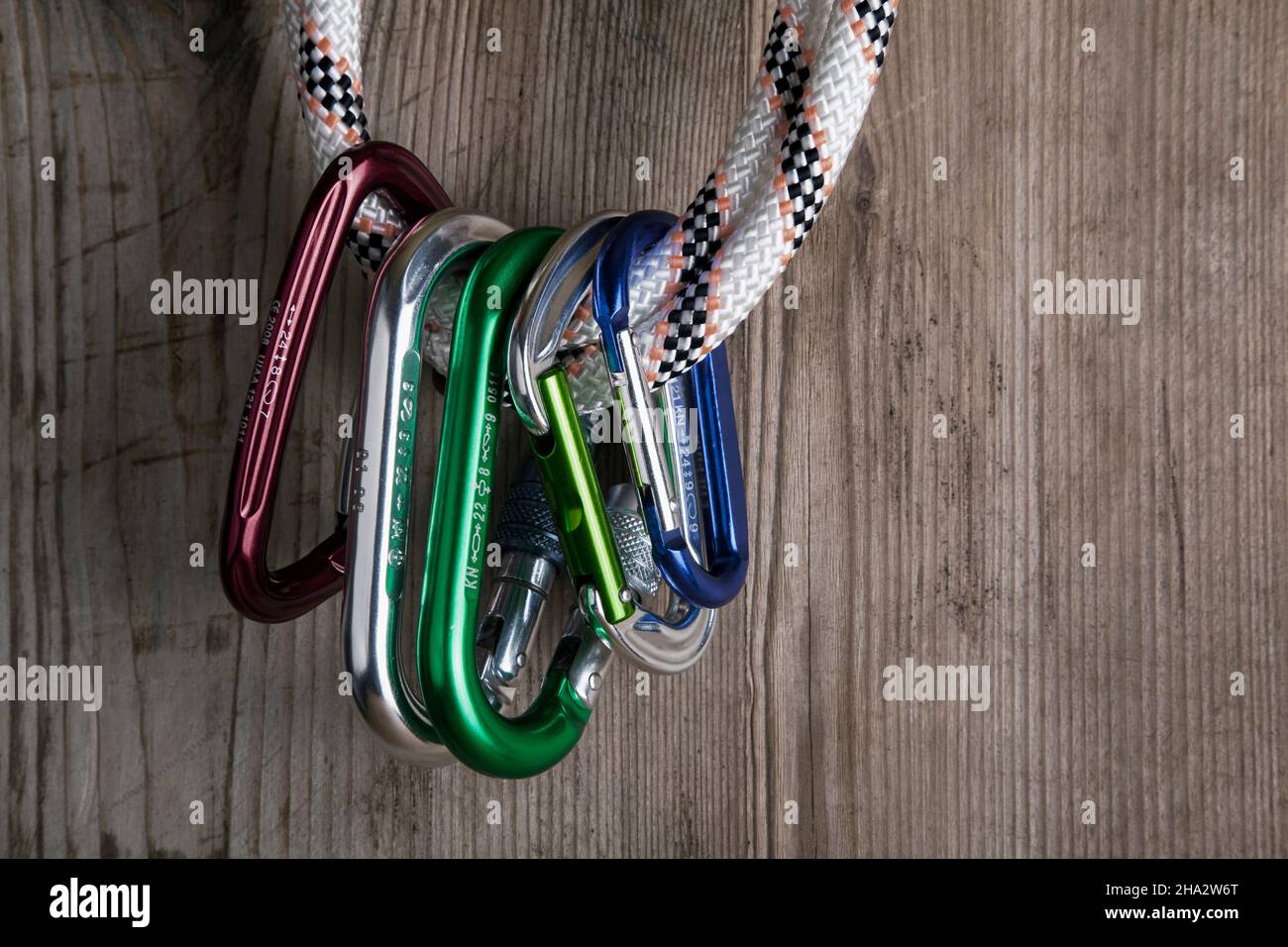 five carabiners hanging on a rope on a wooden wall Stock Photo