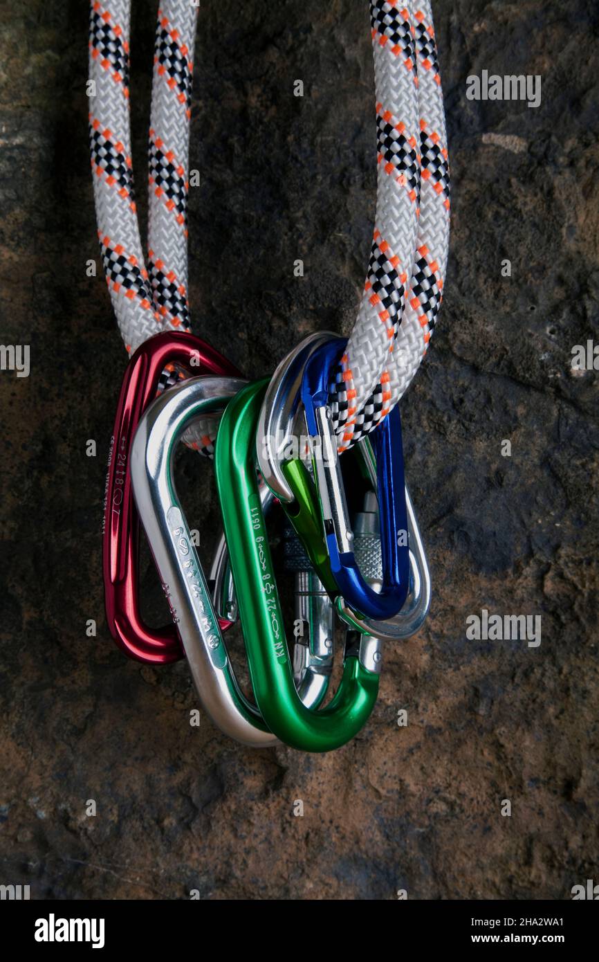 five carabiners hanging on a rope on a rock face Stock Photo