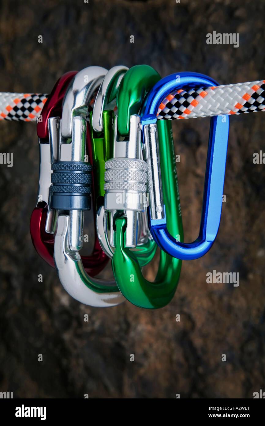 five carabiners hanging on a rope on a rock face Stock Photo