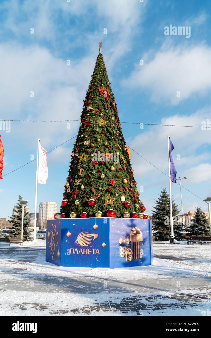 A decorated Christmas tree stands on the city square with the inscription Planet, in Russian, on a pedestal on a sunny day. Stock Photo