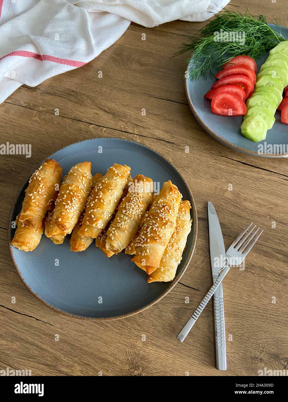 A classic Turkish breakfast table is seen in close-up.  Delicious homemade spring rolls and fresh tomatoes and cucumbers stand on plates. Stock Photo