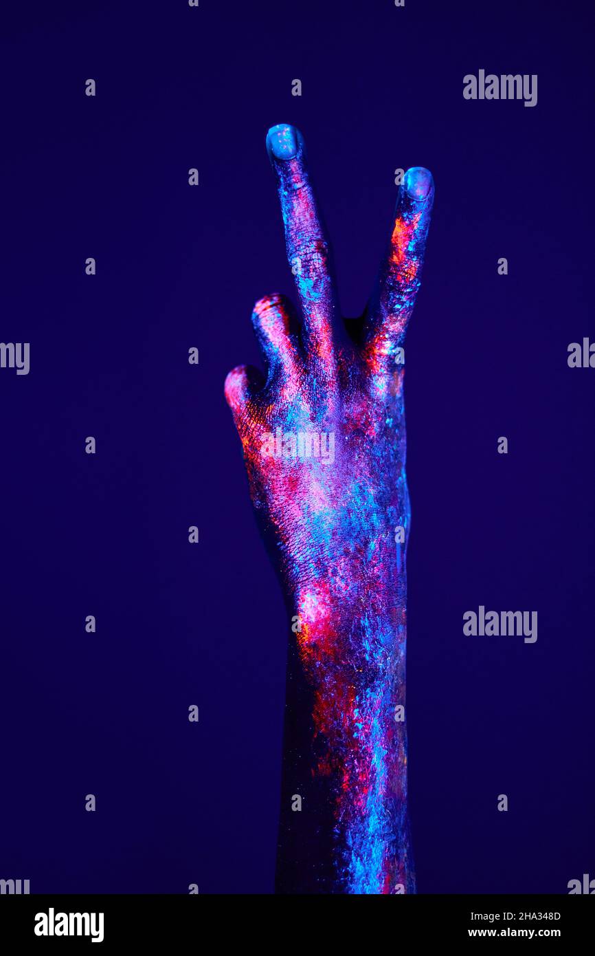 The gesture of victory, hand with fluorescent colorful painting on neon ...