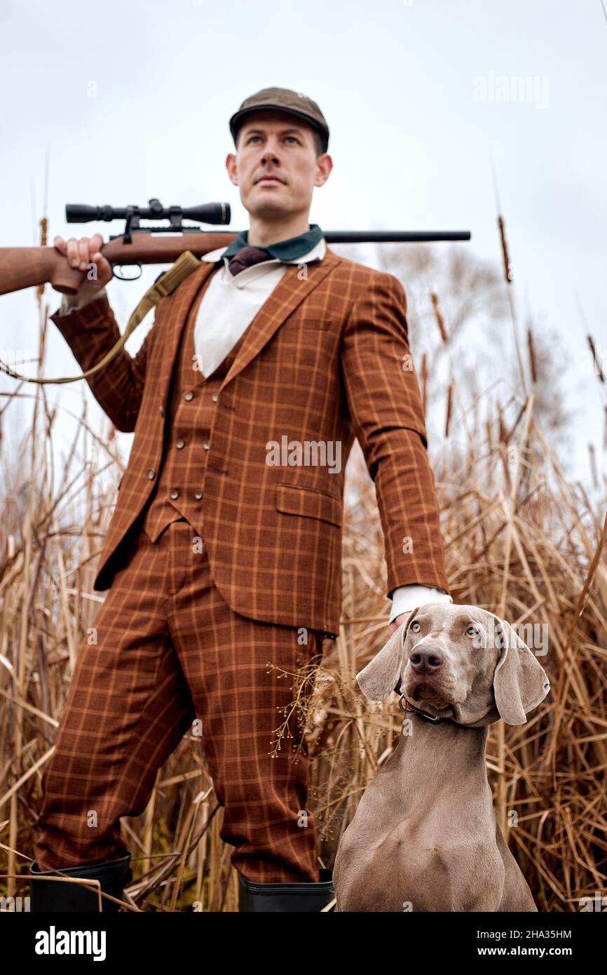 portrait of handsome guy in suit with gray dog on hunting, looking at side. down view. caucasian american guy with purebred dog standing among high au Stock Photo