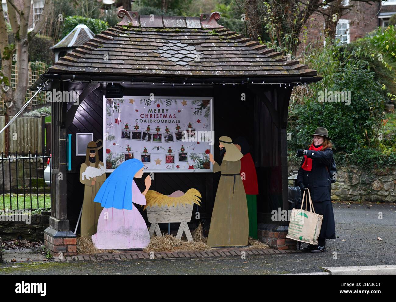 Shropshire, UK. 10th Dec, 2021. Coalbrookdale, Shropshire, Uk December 10th 2021. No room at the shelter! A commuter waiting at the village bus stop in Coalbrookdale, Shropshire stands outside the bus shelter as it is now locating the school Christmas Nativity Scene. Credit: David Bagnall/Alamy Live News Stock Photo