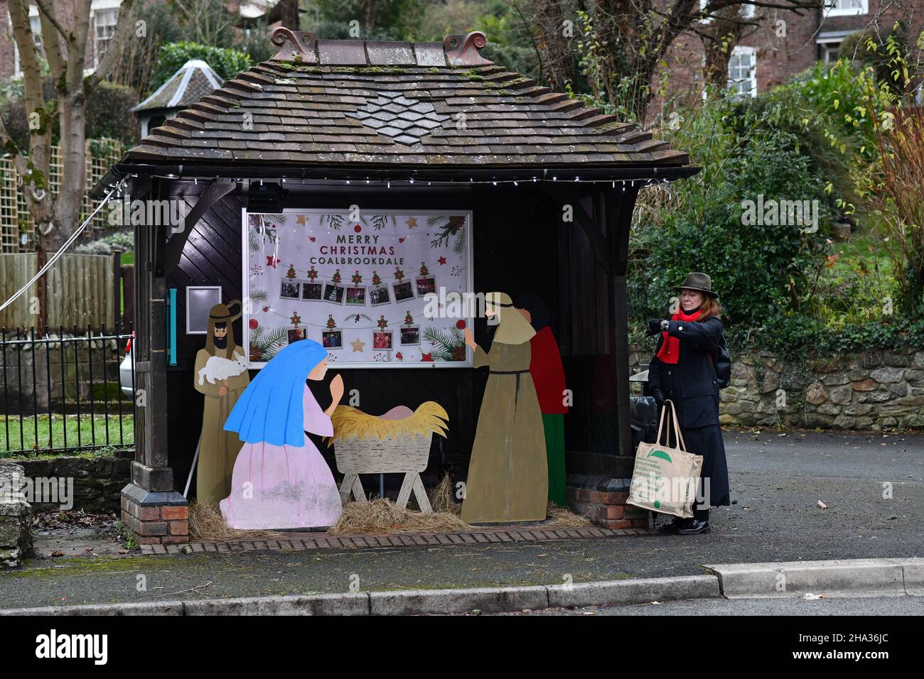 Shropshire, UK. 10th Dec, 2021. Coalbrookdale, Shropshire, Uk December 10th 2021. No room at the shelter! A commuter waiting at the village bus stop in Coalbrookdale, Shropshire stands outside the bus shelter as it is now locating the school Christmas Nativity Scene. Credit: David Bagnall/Alamy Live News Stock Photo