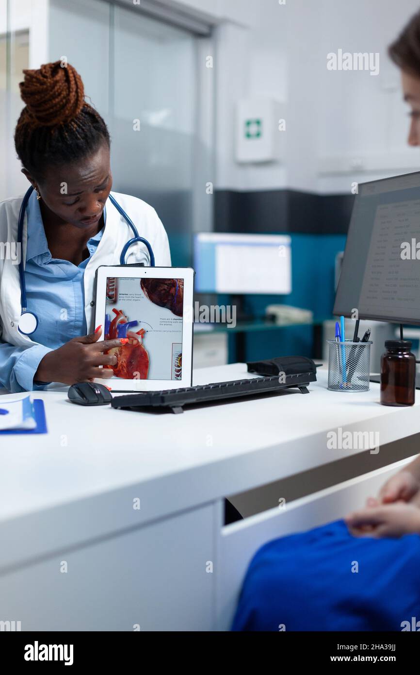 African american radiologist doctor holding tablet explaining heart radiography discussing medical expertise with patient woman during clinical appointment. Cardiologist working in hospital office. Stock Photo