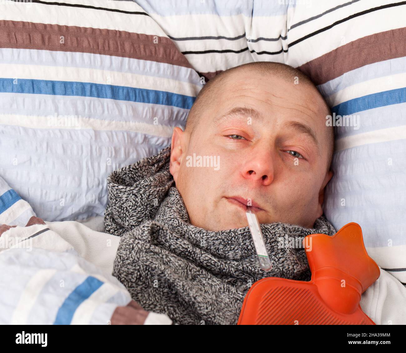 Sick man with a hot water bottle and thermometer sickness, flu, colds, person, human, red, nose, cold, lying, sick, slee Stock Photo