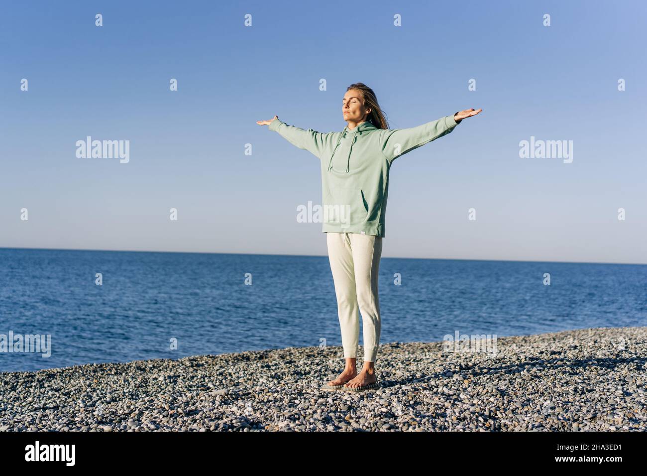 Woman doing energy yoga practice by the sea while standing on boards with nails. Stock Photo