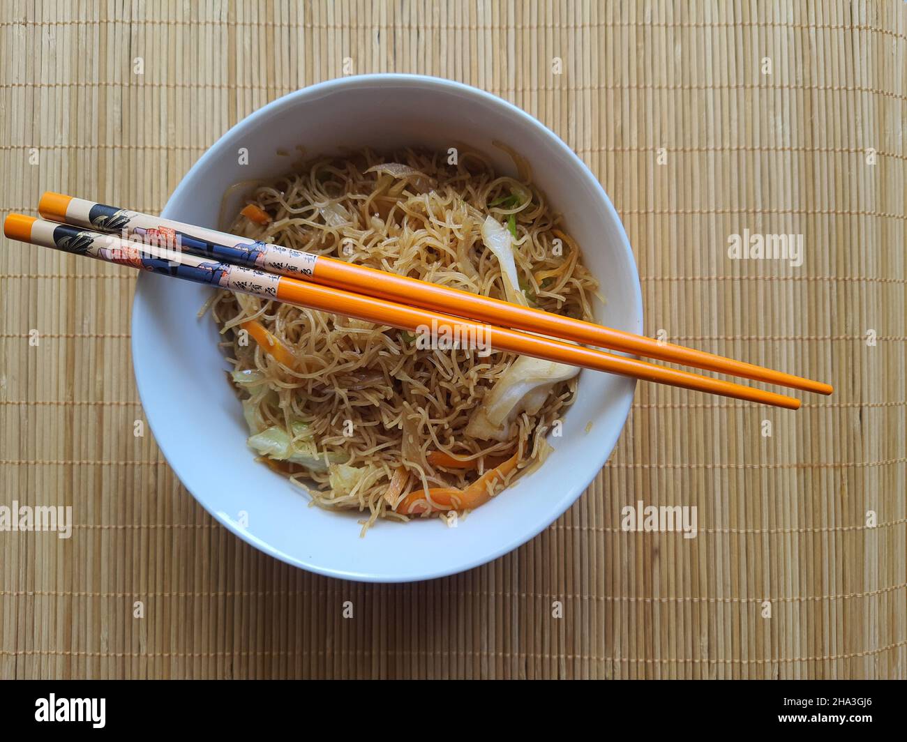 Bifum vegetable noodles in a white crockery bowl with two chopsticks on a bamboo placemat. View from above. Stock Photo