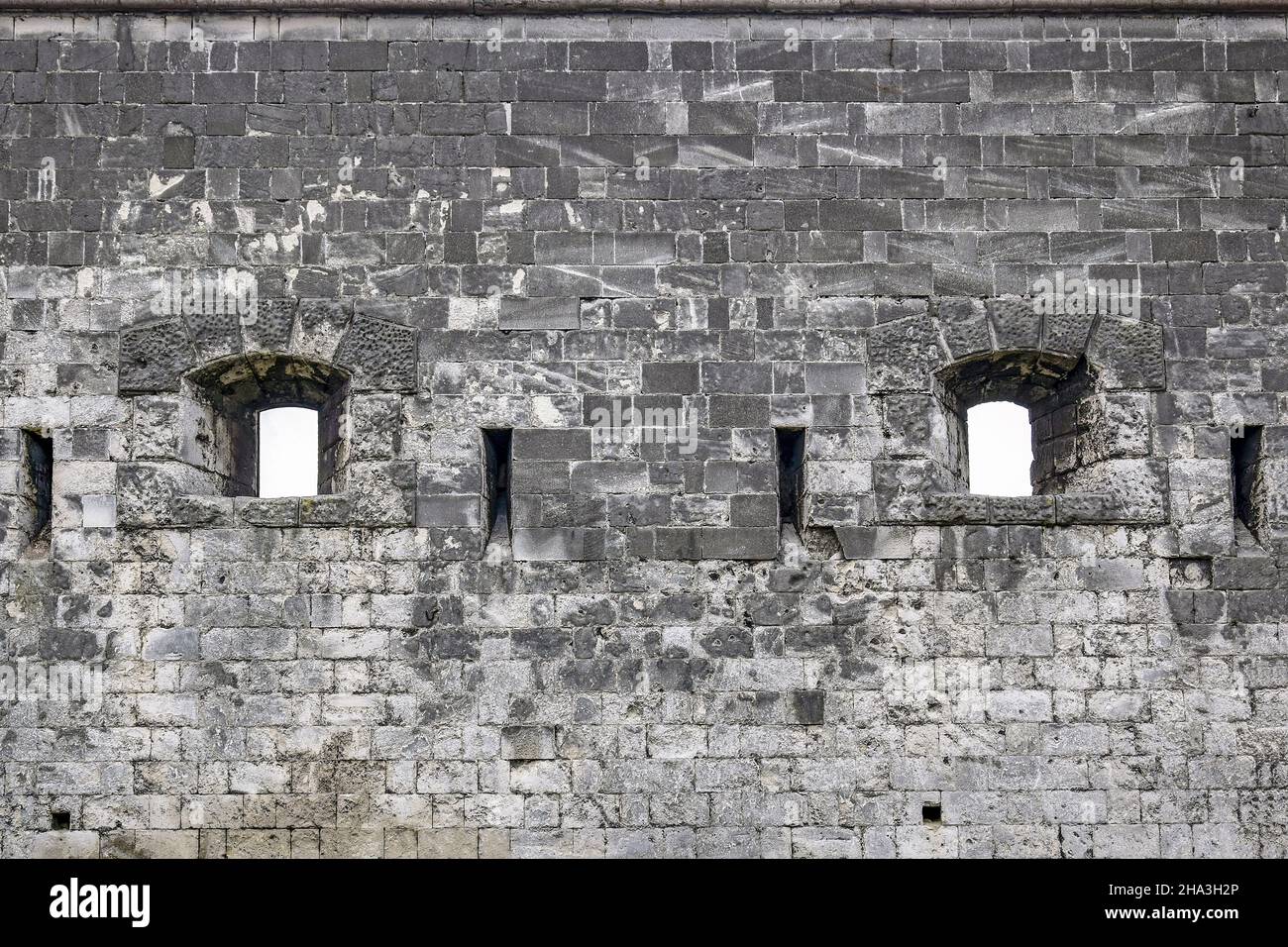Stone wall of an ancient castle with windows in the form of loopholes. Close-up. Selective focus. Copy space. Stock Photo