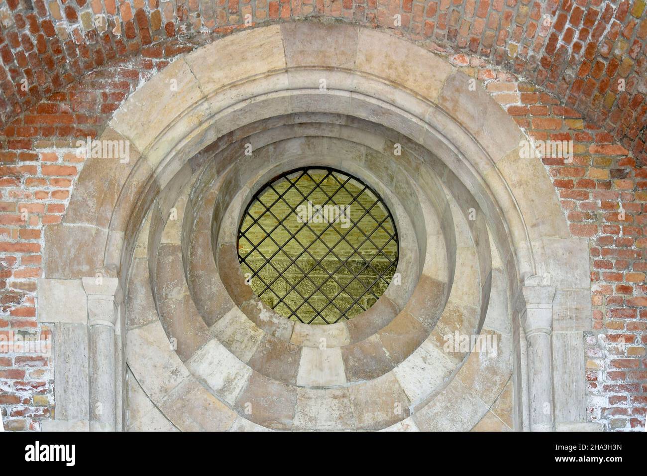 Round window with iron bars in an old brick temple. Arched decor of ...