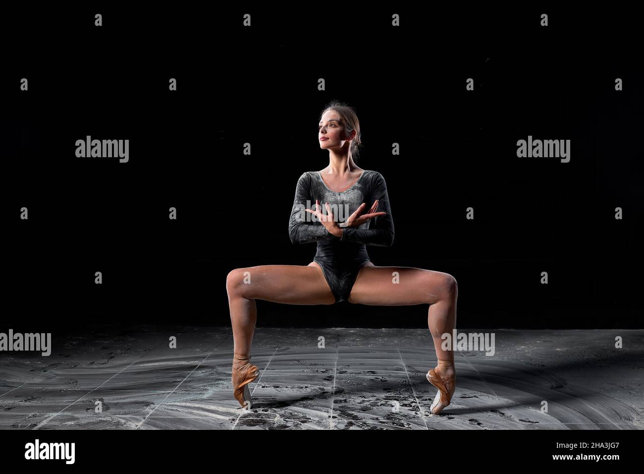 Flexible woman dancing on black background in studio, moving with legs apart. Talented caucasian athlete ballet dancer in bodysuit in slow motion, loo Stock Photo