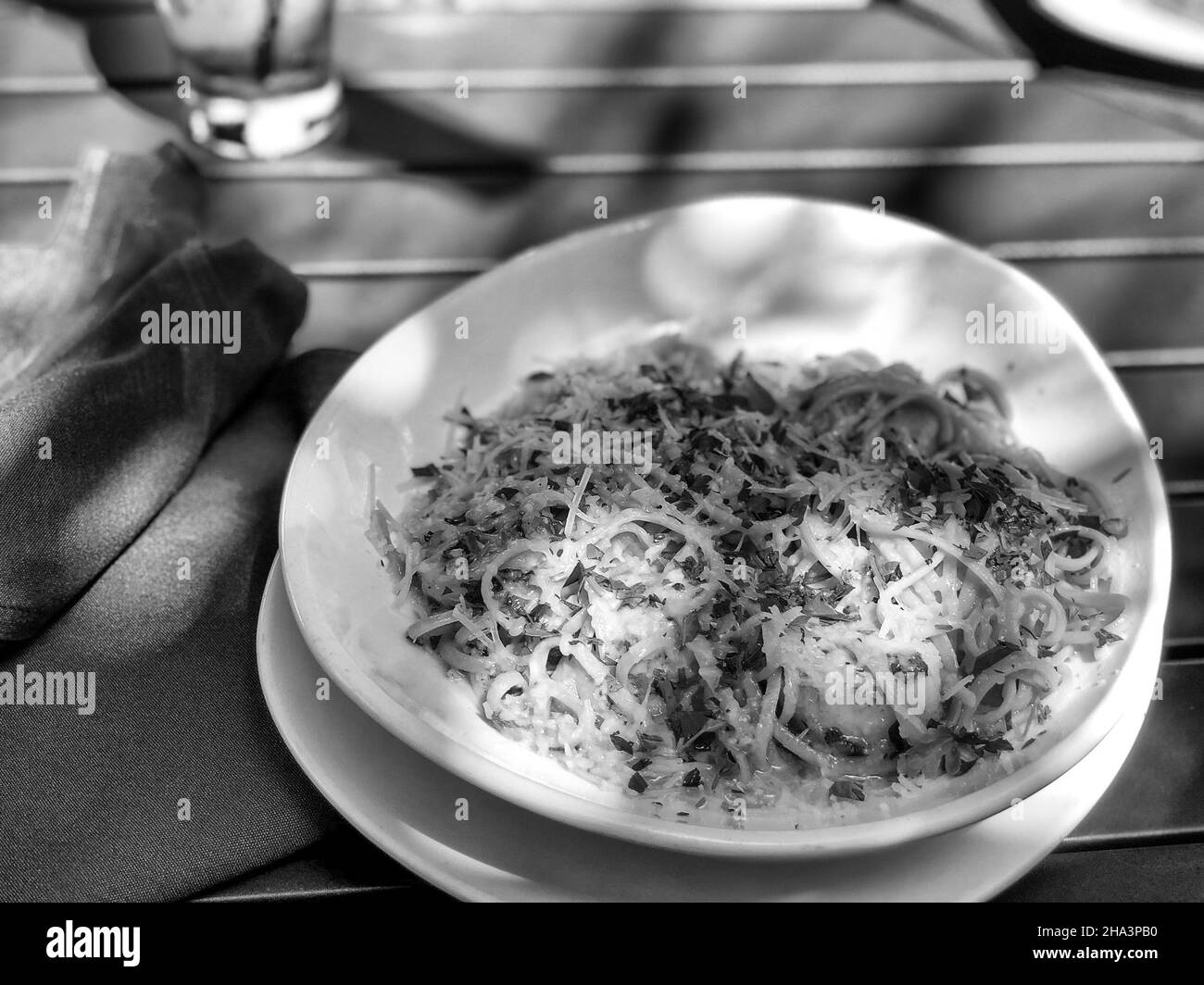 Grayscale shot of pasta spaghetti with cheese on a wooden table of an outdoor cafe Stock Photo