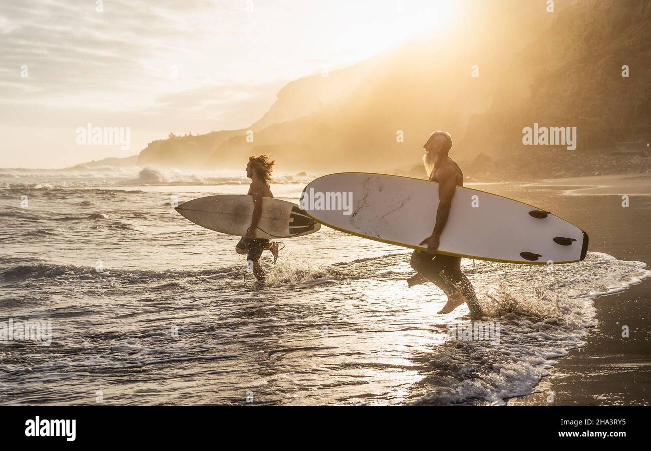 Happy fit friends surfing together on tropical beach at sunset time - People lifestyle and extreme sport concept Stock Photo