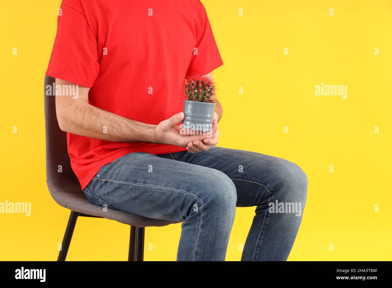 Man sitting on chair on yellow background. Hemorrhoids concept Stock