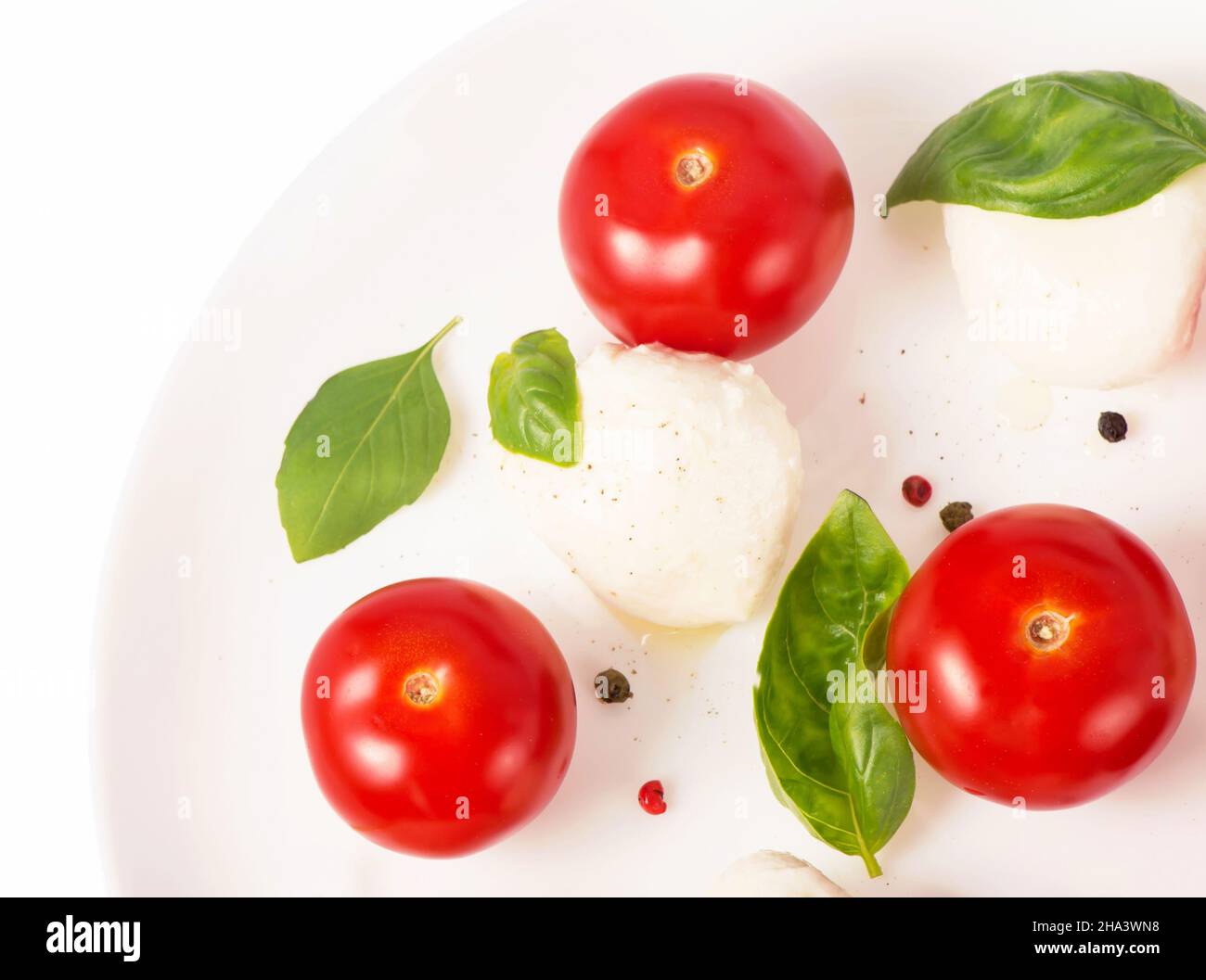 Round camembert cheese with cherry tomatoes and basil on a white plate. Stock Photo