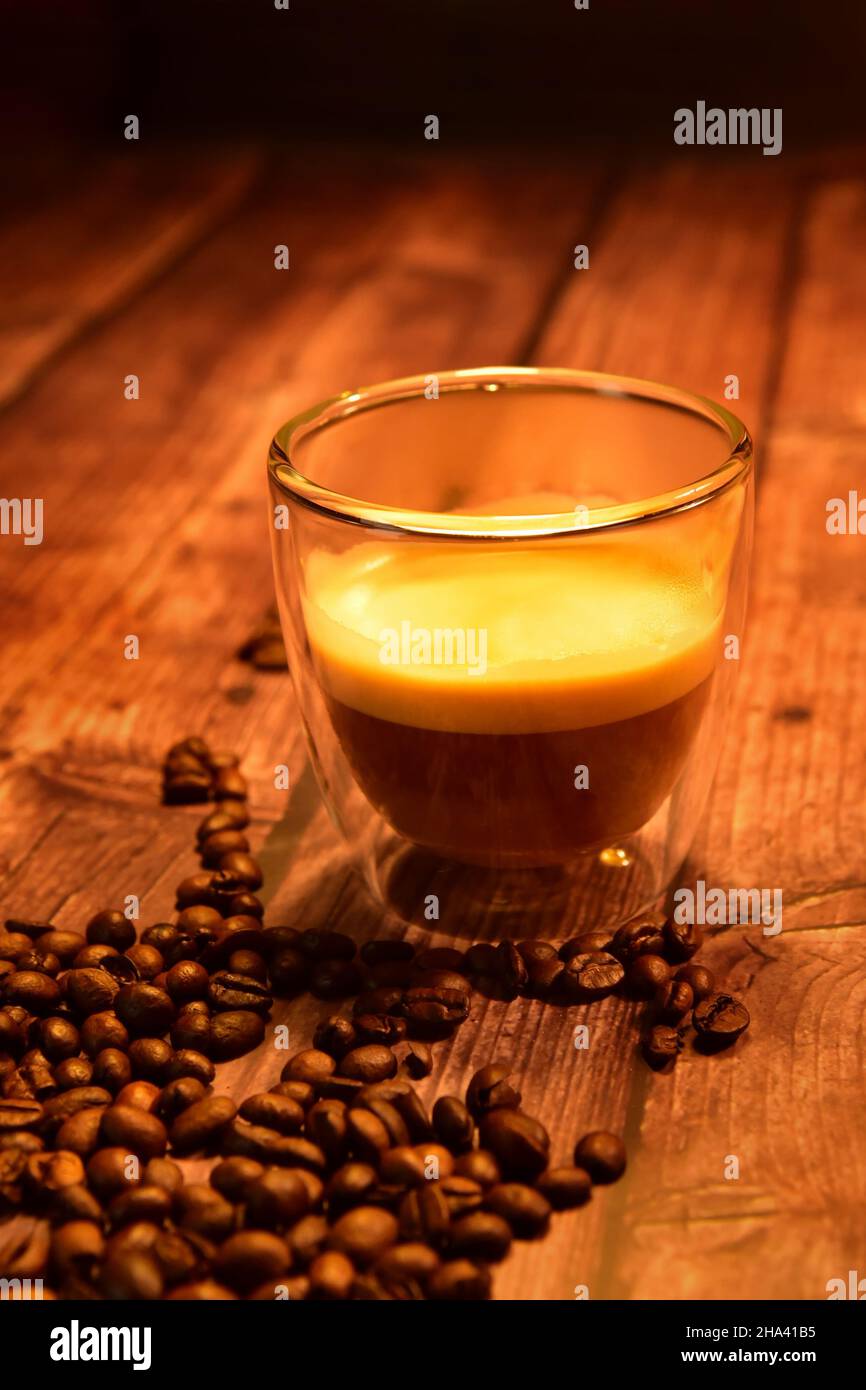 Front view of a glass cup of delicious coffee on a rustic wooden table with coffee beans. Stock Photo