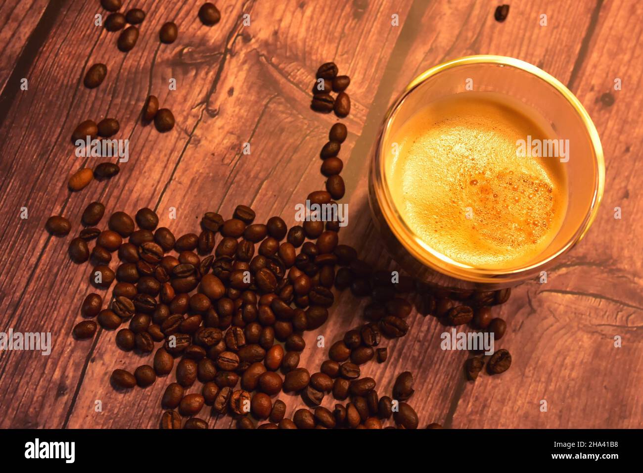 Top view of a glass cup of delicious coffee on a rustic wooden table with roasted coffee beans. Stock Photo