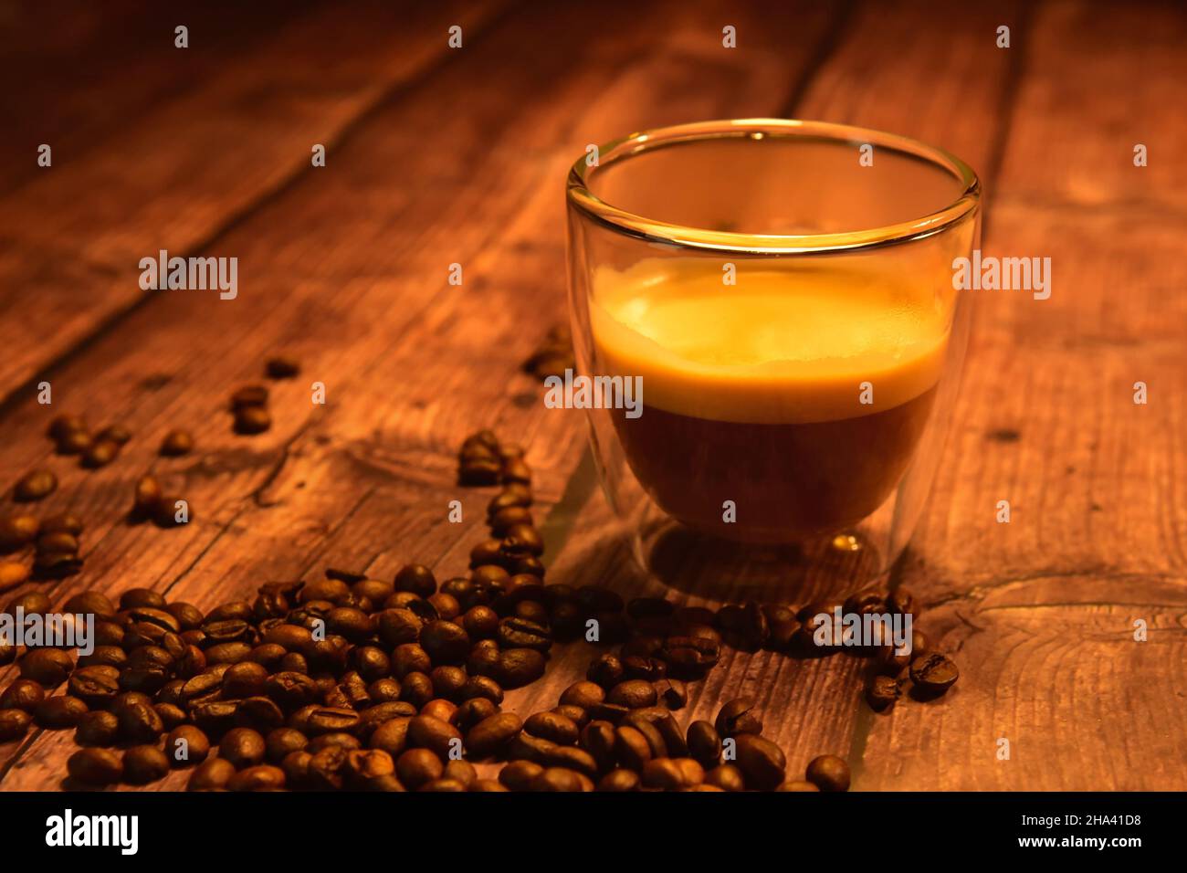 Front view of a glass cup of coffee with crema on a rustic wooden table with roasted coffee
