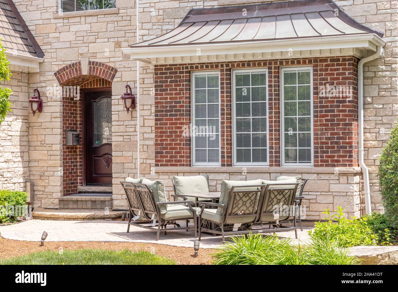 A brick patio of a luxury, stone home with chairs sitting around a table. Stock Photo