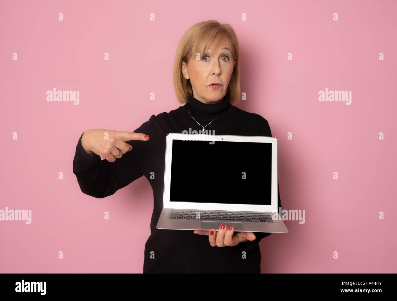 Senior woman showing laptop computer screen isolated over pink ...
