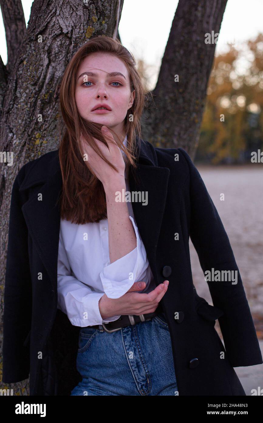 Long straight haired white european woman in dark coat near the tree Stock Photo