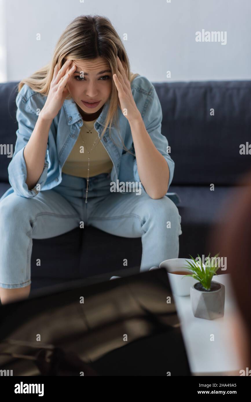 frustrated woman holding hands near head while sitting near blurred psychologist Stock Photo