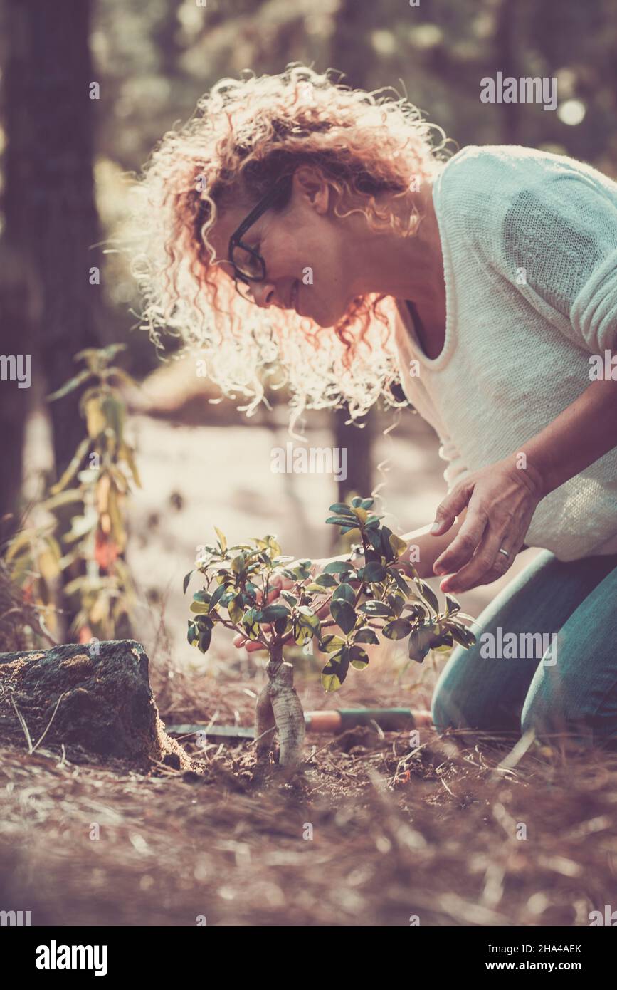 smiling woman with curly hair planting new tree in forest or garden. happy woman taking care of plant in nature. woman celebrating earth day Stock Photo